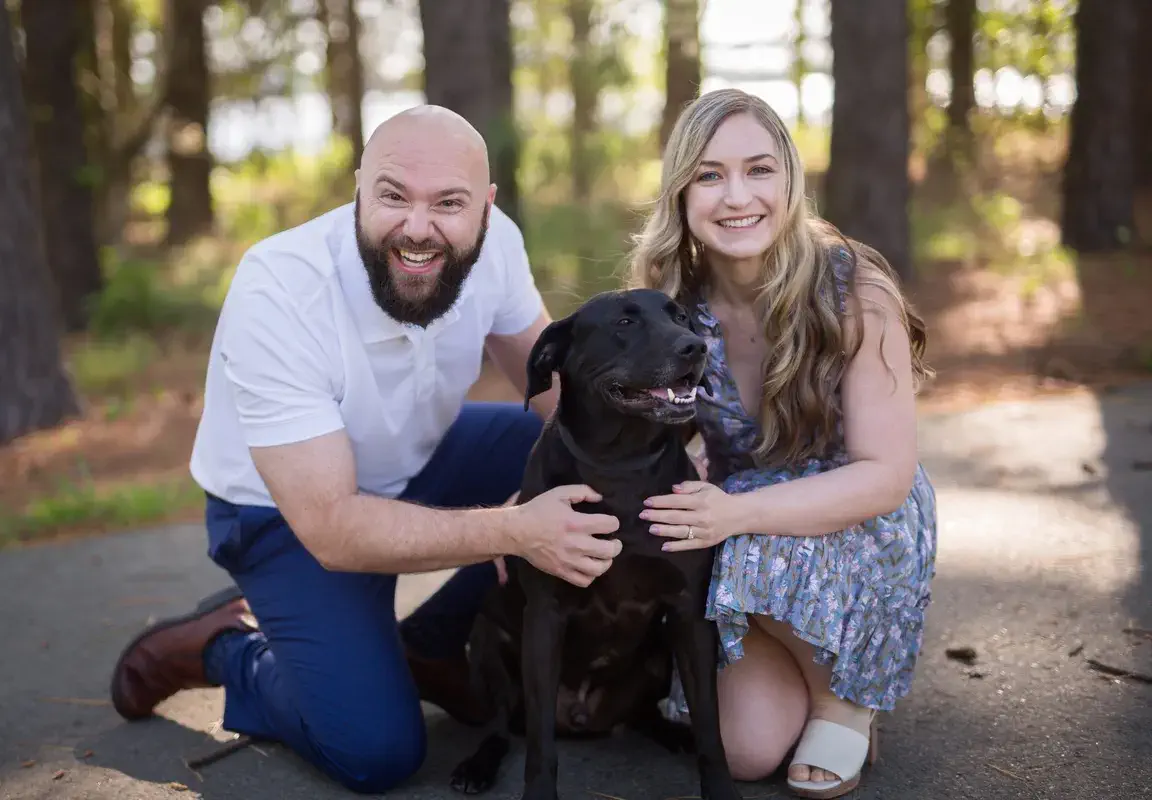 Engaged couple and their dog sitting together in a field at Two Rivers Park, Little Rock